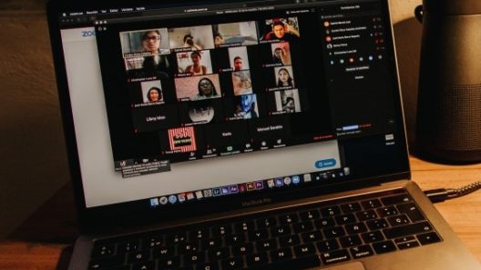 Laptop on a desk running a Zoom call with multiple faces on the screen