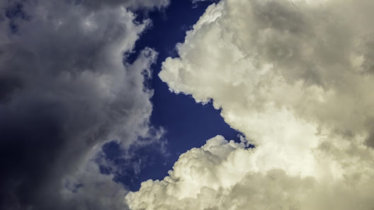 Rift between shadowy cloud at left and towering cumulus cloud at right on a summer evening, for background or element with motifs of difference, instability, changeability