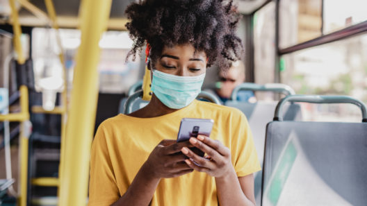 woman wearing a protective mask while sitting in a bus and using a mobile phone