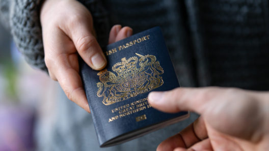 A close up of a hand passing a British passport to someone else.