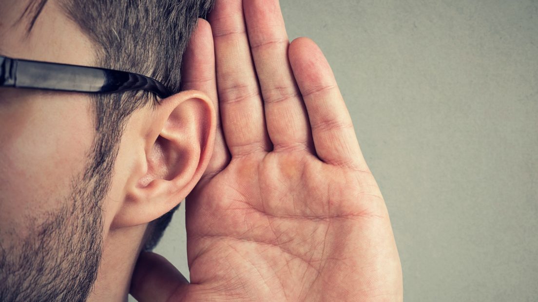 man holds his hand near ear and listens carefully isolated on gray wall background