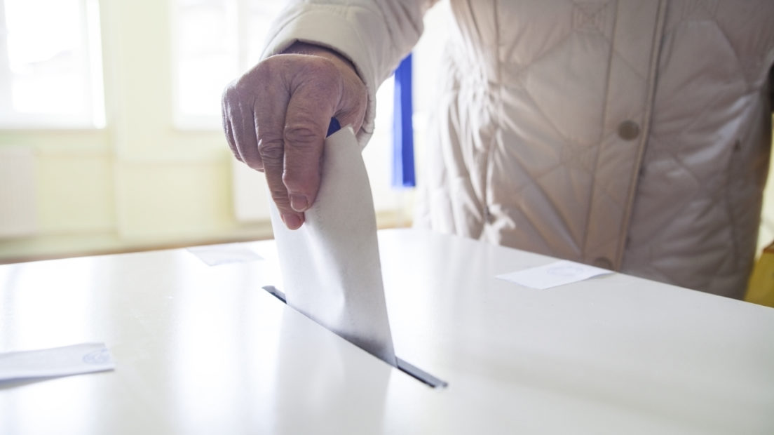 Hand of a person casting a ballot at a polling station during voting.