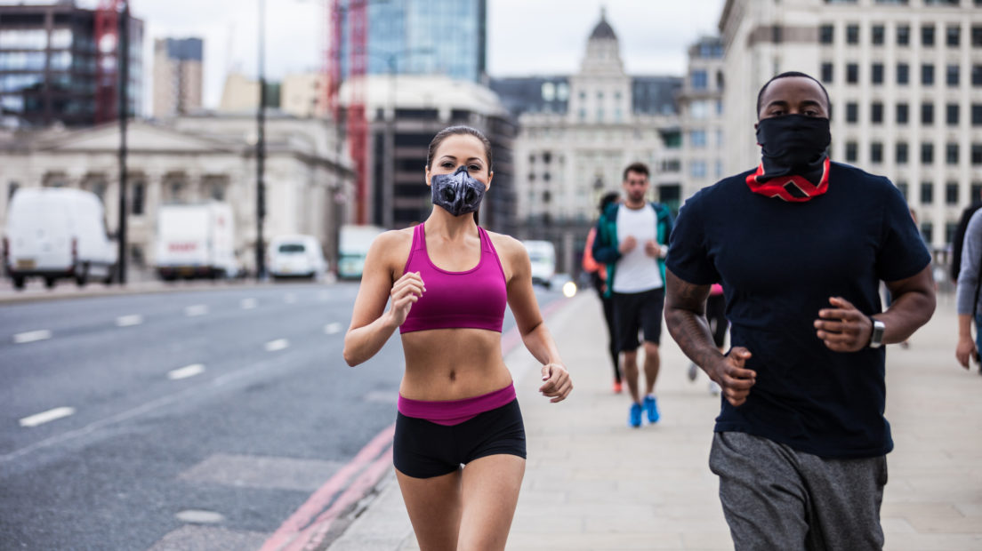 A man and a woman jogging on the pavement in a city. They are wearing face masks to protect from pollution.