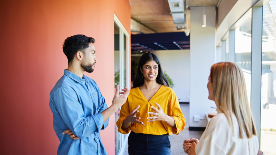 Three people (two women and a man) standing in a hallway having a conversation.