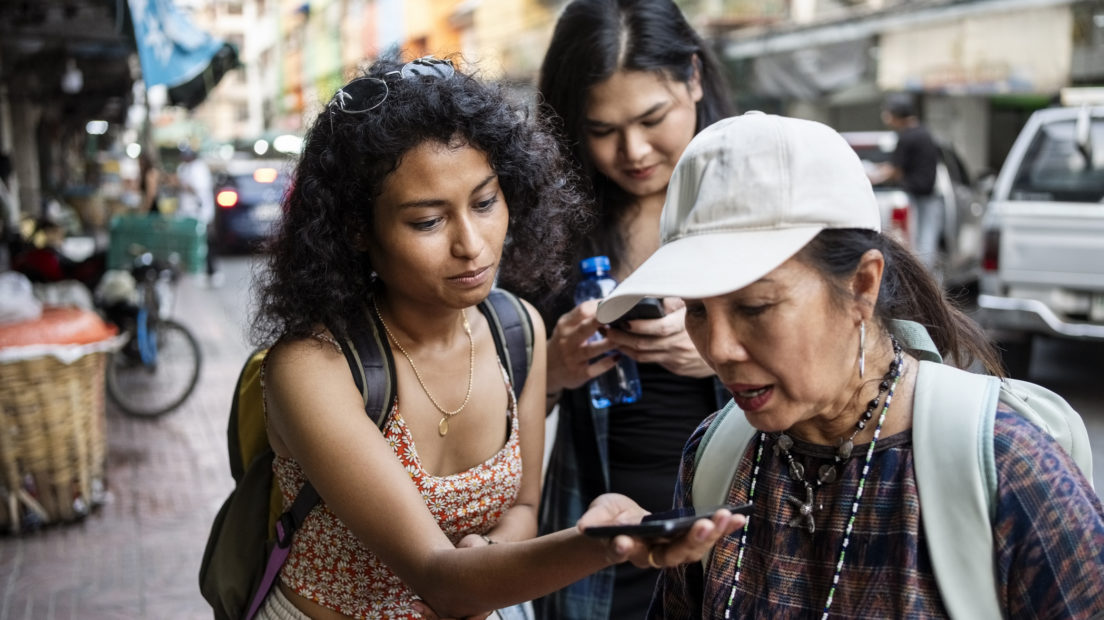 Female tourists holds a phone out for their tour guide to translate during a city tour