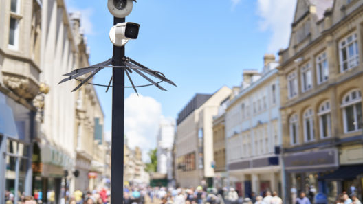 A CCTV security camera mounted on a post overlooking a busy high street