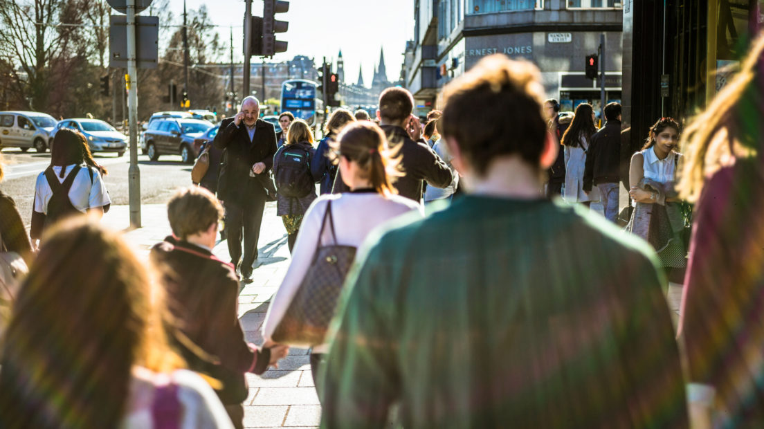 An over-the-shoulder shot of people walking on a central shopping street in Edinburgh on a sunny day in spring.
