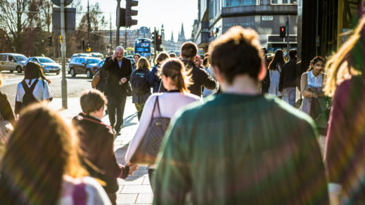 An over-the-shoulder shot of people walking on a central shopping street in Edinburgh on a sunny day in spring.