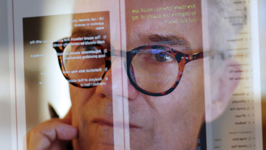 Close up stock photograph of a mature man studying a see-through computer monitor that’s displaying text provided by an AI (artificial intelligence) chatbot.