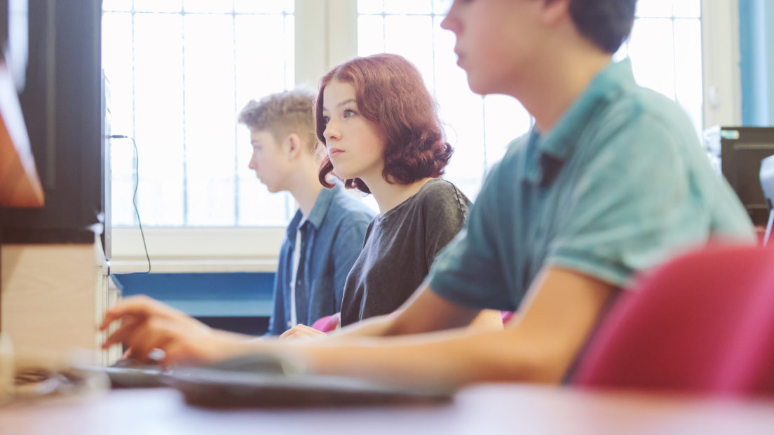 Group of teenagers using computer during automatic programming lesson, sitting in a row in school computer lab.